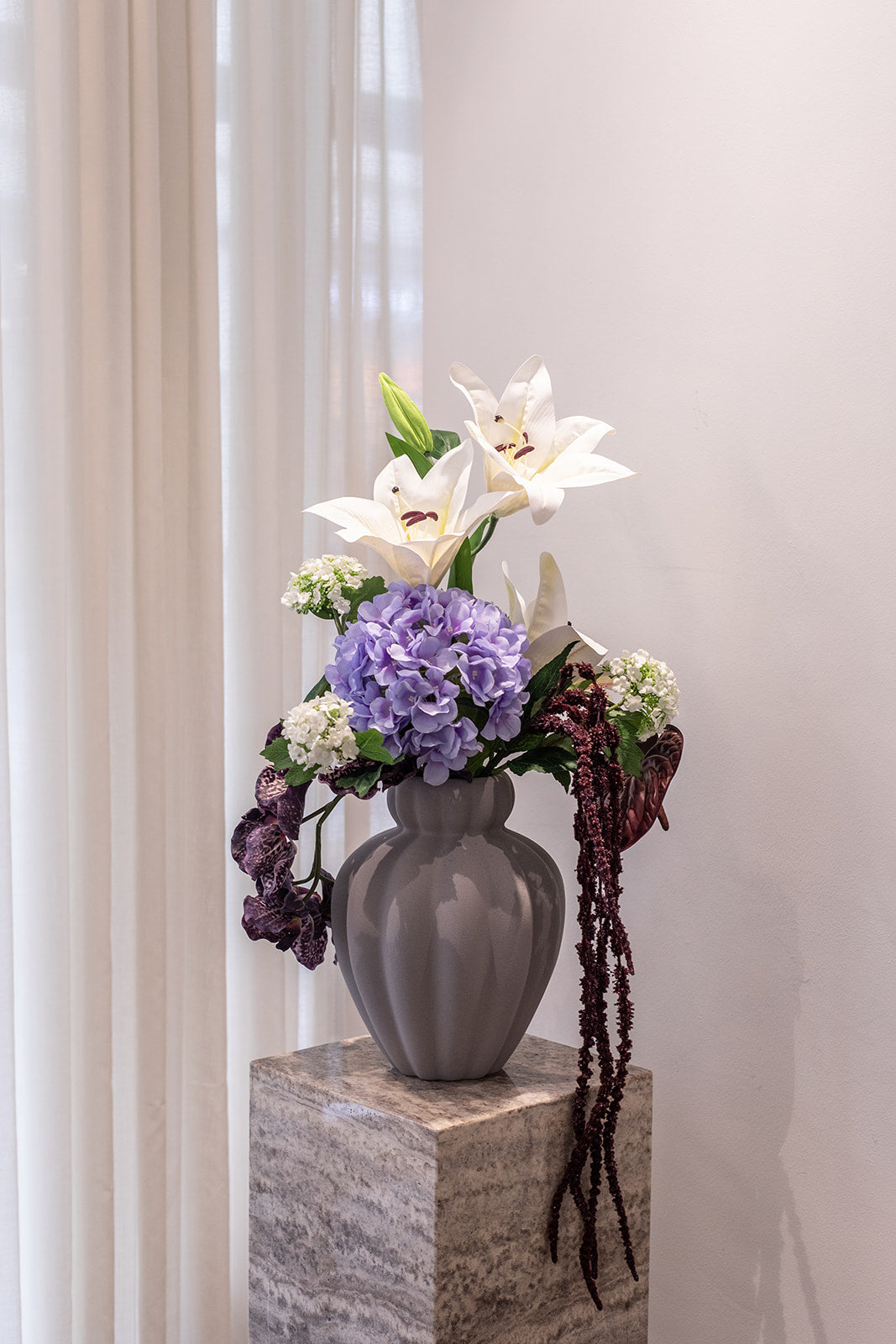 Kunstige blomster sammensat til buket.
Buketten er stylet i den håndlavede Penelope vase i farven grå i størrelsen large.
Buketten indeholder:
1 x Burgundy amaranthus branch
1 x Purple x-large hydrangea
1 x White lily large
1 x White hydgrangea branch
1 x Burgundy orchid (7 heads)
1 x Burgundy anthurium