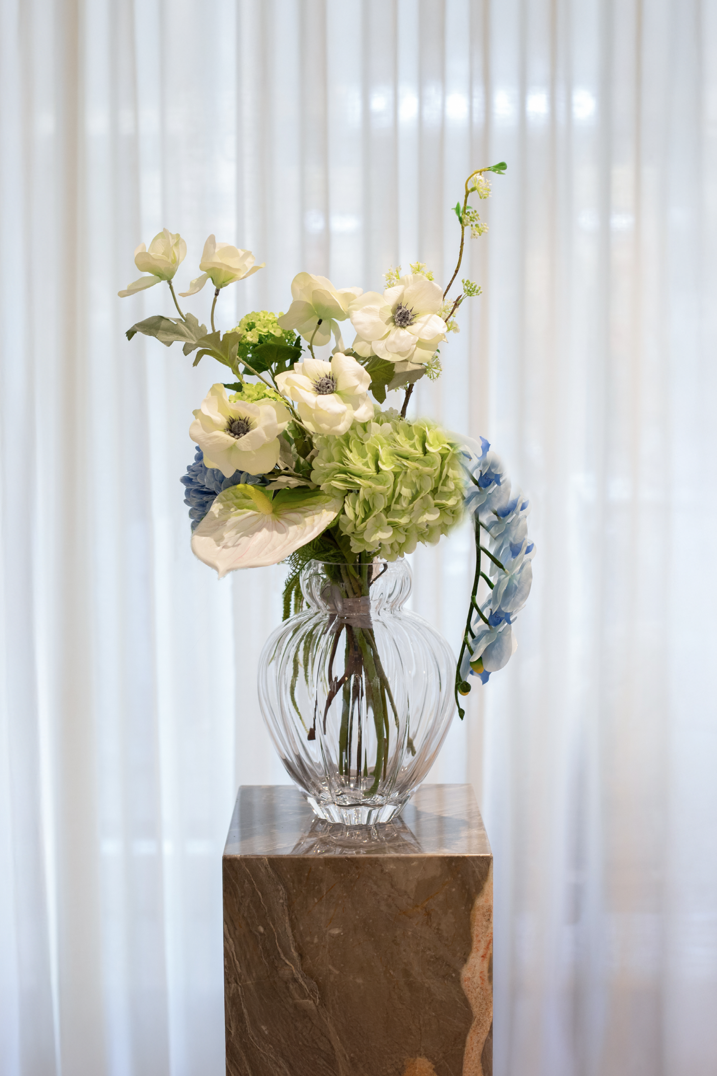 Kunstige blomster sammensat til en buket. Buketten er stylet i den mundblæste Audrey vase i large.
Buketten indeholder
1 x white anthurium
1 x light green hydrangea
1 x blue orchid (9 heads)
2 x white poppy
1 x blue hydrangea
1 x white fontanesia
1 x light green hydrangea branch