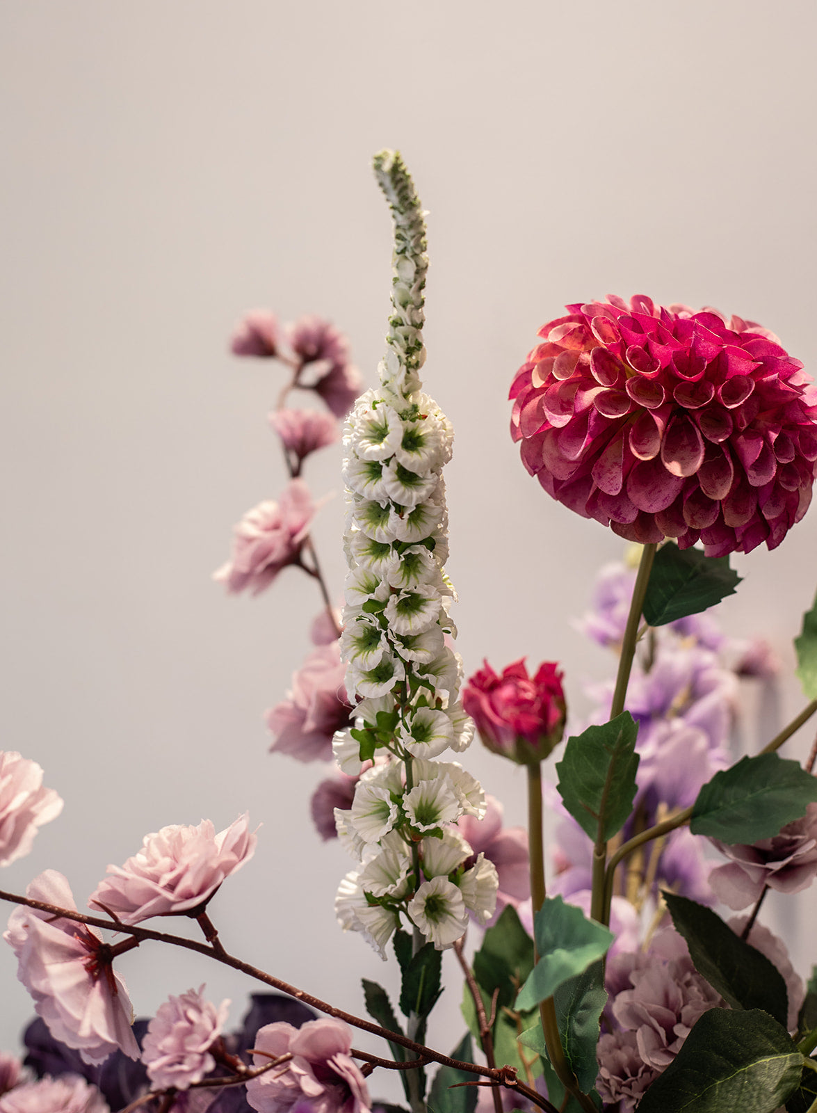 Kunstig buket Rosenglød med hvide og lilla orkidéer, pink dahlia, kirsebærblomster og lilac branch – fyldig og farverig blomsterbuket i silkelook.