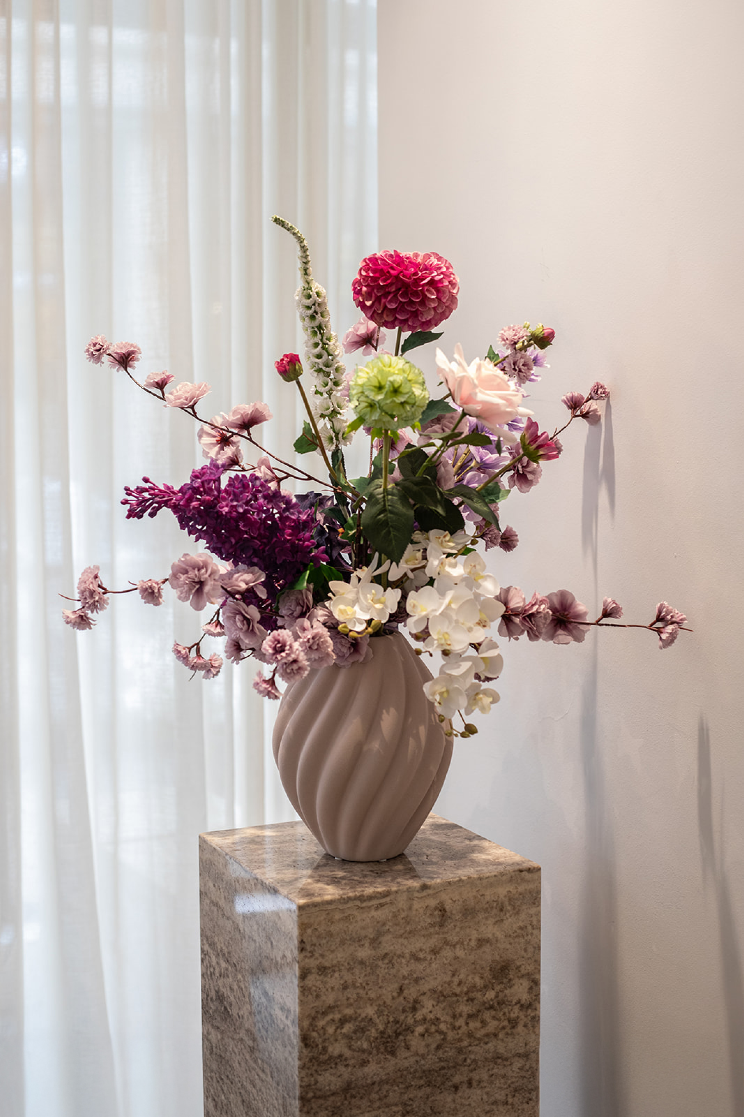 Kunstig buket Rosenglød med hvide og lilla orkidéer, pink dahlia, kirsebærblomster og lilac branch – fyldig og farverig blomsterbuket.