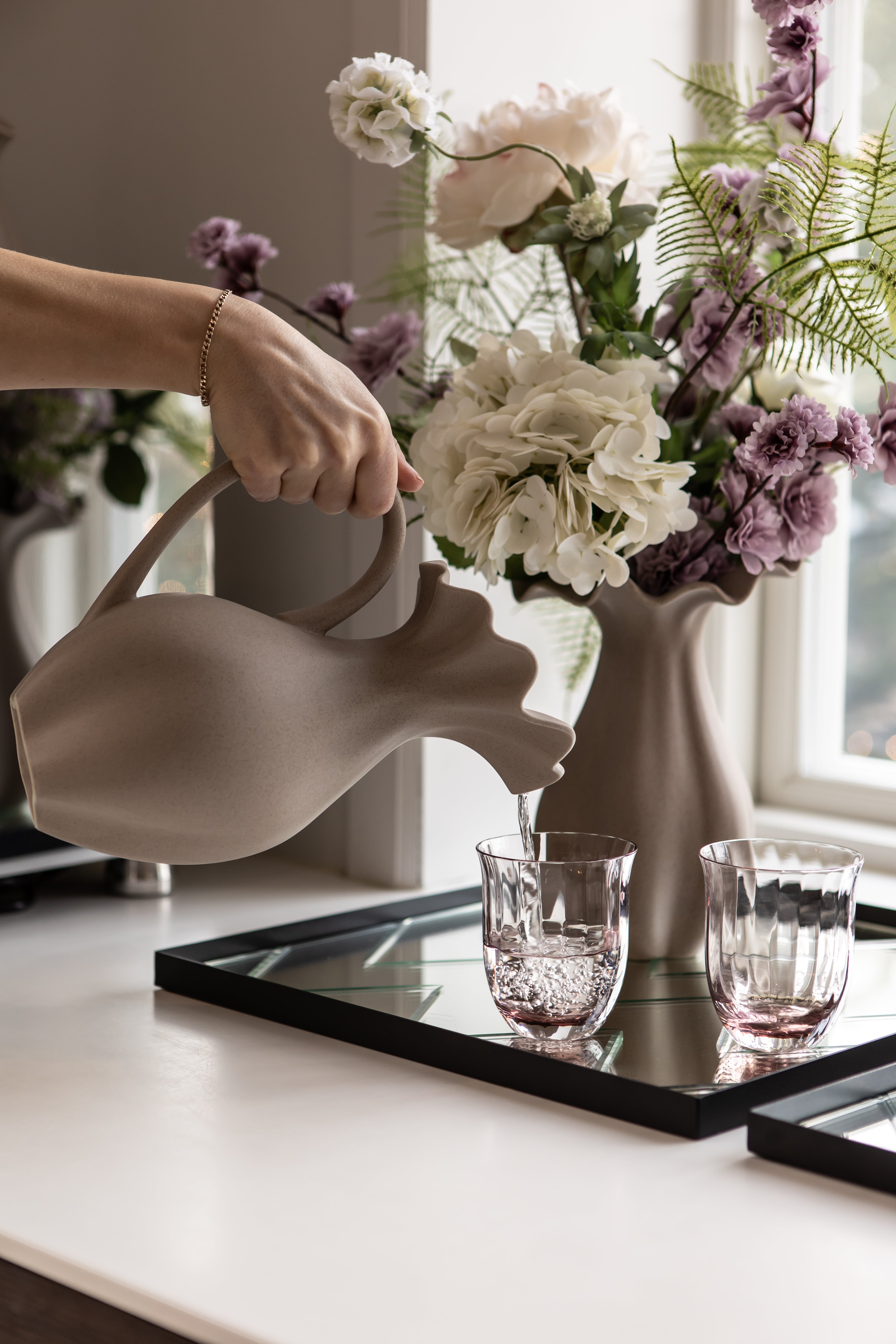 keramik kande med drikkeglas og kunstige blomster. stylet i vindueskarm på spejlbakke.